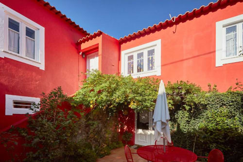 Pátio da villa SOTAM Country House com paredes vermelho vibrante, janelas com moldura branca, sebes cobertas de hera e móveis de pátio vermelhos