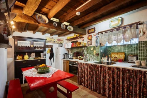Cozinha rústica da quinta SOTAM Country House com mesa de jantar vermelha, vigas aparentes, azulejos verdes e estilo português tradicional