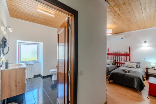 Suíte moderna na SOTAM Country House com layout aberto conectando quarto com cabeceira vermelha e banheiro, tetos de madeira,