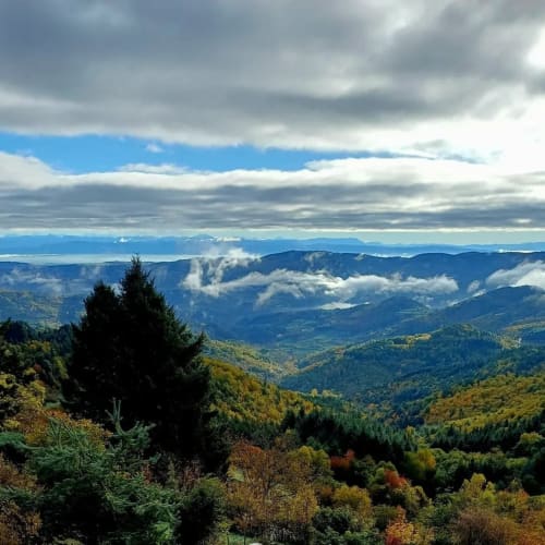 Montagnes et vallées boisées ondulantes en Ardèche, France, avec un ciel nuageux dramatique et des pics lointains