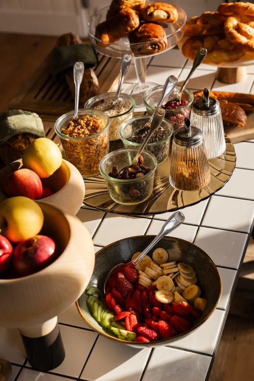 Breakfast spread at Moulin Moulin B&B in Dannes with fresh fruits, pastries, cereals, and toppings on white tiles.