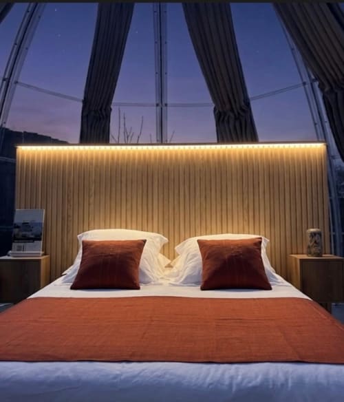 Chambre Bubble Jade Topaze avec tête de lit illuminée, coussins couleur rouille et vue sur jardin par les baies vitrées cintrées au crépuscule