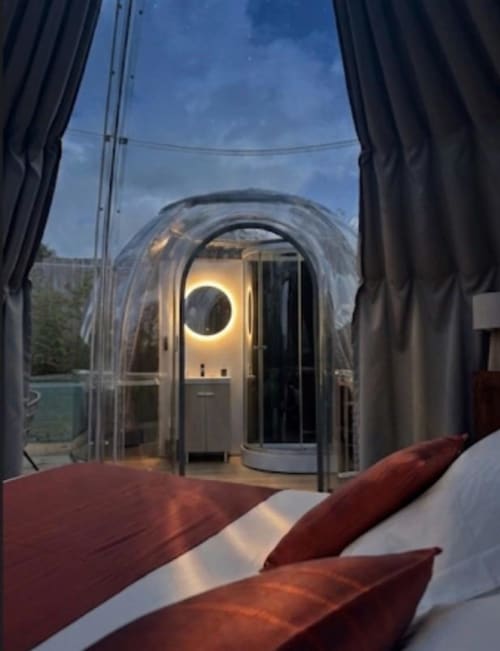Chambre de l'hôtel Bubble Jade avec baie vitrée circulaire illuminée, vue sur le jardin, literie rouge et jacuzzi privé