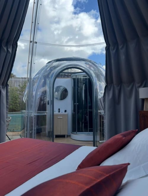 Chambre Bubble Jade avec structure en dôme transparent offrant une vue sur le jardin, literie bordeaux et terrasse extérieure