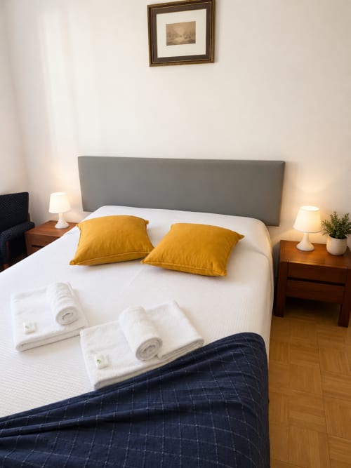 Serrana Gerês Inn bedroom with gray headboard, yellow pillows, white bedding, wooden nightstands, and framed artwork in