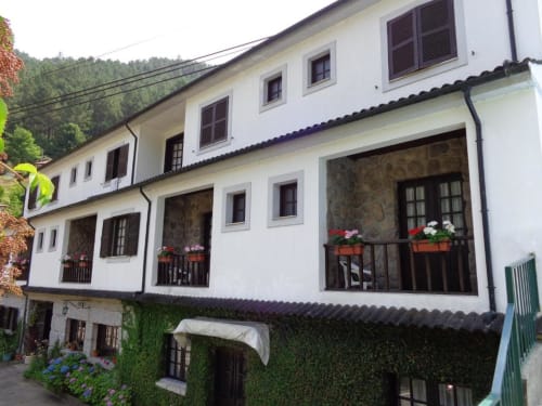 Serrana Gerês Inn hotel facade in Gerês, Portugal with white walls, wooden balconies, flower boxes, and forested mountain