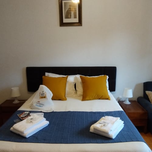 Hotel bedroom at Serrana Gerês Inn with black headboard, white bedding, gold pillows, and towel sets on navy blue runner