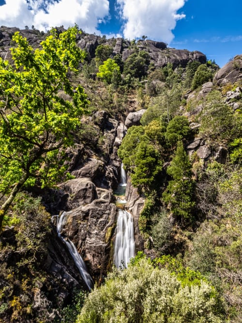 Cascading waterfall through lush green forest and rocky cliffs at Serrana Gerês Inn in Portugal