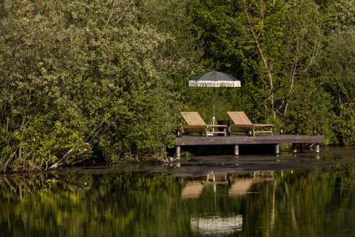 Ponton en bois avec chaises longues et parasol sur une eau calme, entouré de verdure luxuriante au Moulin Moulin B&B à Dannes