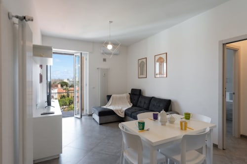Moderno soggiorno con divano nero, tavolo da pranzo e terrazza con vista sul mare al Welcome Holiday, Finale Ligure