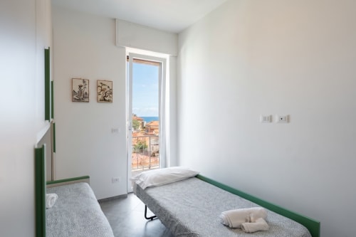 Camera luminosa dell'appartamento Maestrale a Varigotti con letti gemelli, cornici verdi, balcone con vista sul mare e paesaggio costiero