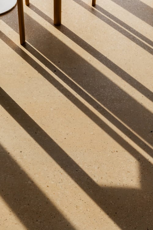 Sol en béton baigné de soleil avec ombres diagonales et pieds de table en laiton à la Moulin Moulin B&B, Dannes