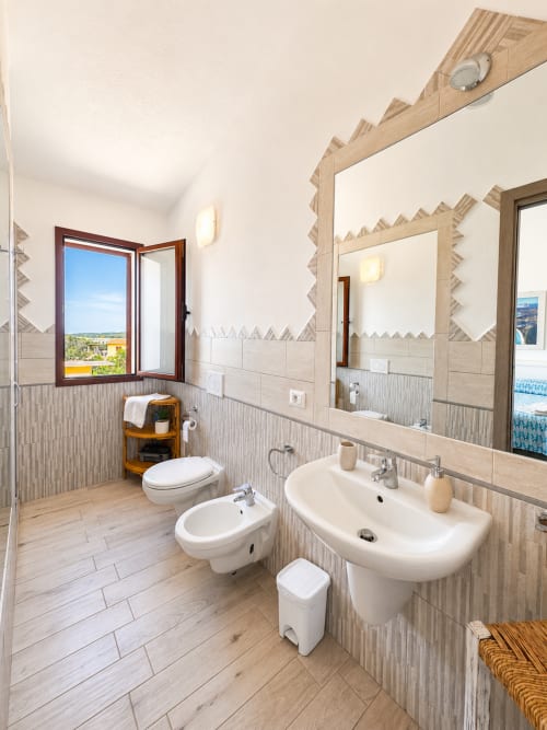 Modernes Badezimmer im Molti Mari B&B in Olbia mit Doppelwaschbecken, Bidet, Toilette, Holzakzenten und Fenster mit Meerblick