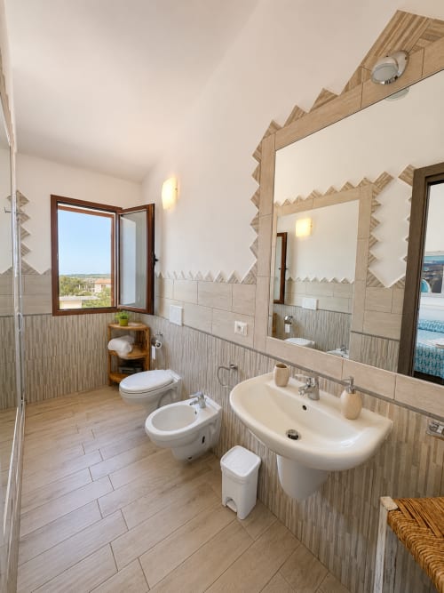 Geräumiges Badezimmer im Molti Mari B&B in Murta Maria mit Doppelwaschtisch, Bidet, Toilette und Fenster mit Meerblick
