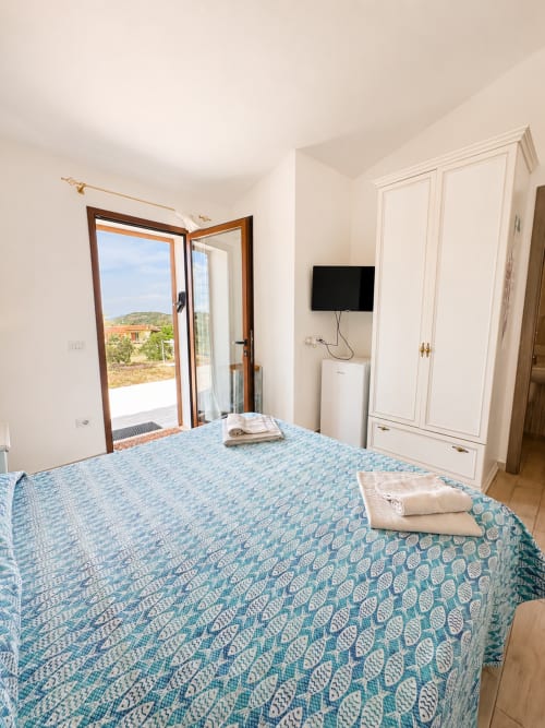 Helles Zimmer im Molti Mari B&B in Olbia mit Meerblickbalkon, blauem gemustertem Bettüberwurf und modernen Annehmlichkeiten