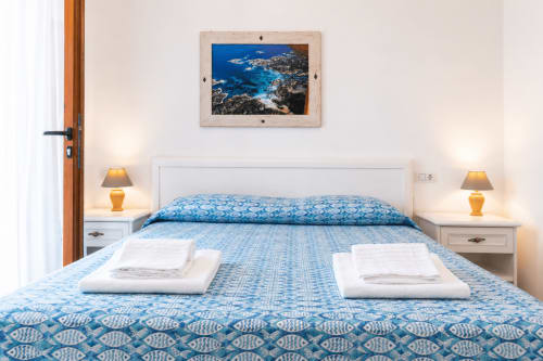 Helles Schlafzimmer im Molti Mari B&B in Olbia mit gemusterter blauer Bettwäsche, Meereskunst und Küstenflair
