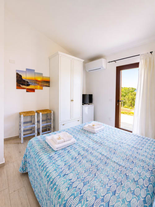 Helles Zimmer in der Molti Mari B&B in Murta Maria mit blaugemustertem Bett, weißem Kleiderschrank, Meerblick-Balkon und Küstensuntergang