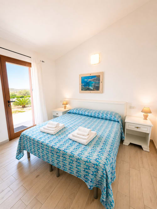 Helles Schlafzimmer im Molti Mari B&B auf Sardinien mit blauem Musterbedding, Meerblick und Terrassenzugang