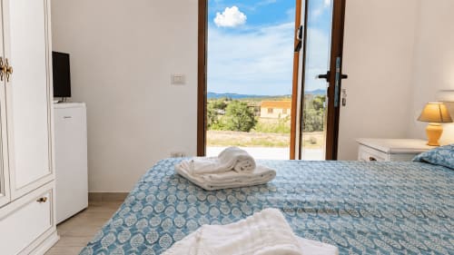 Helles Schlafzimmer mit blauem gemustertem Bettzeug im Molti Mari B&B auf Sardinien, Meerblick mit Terrassentüren