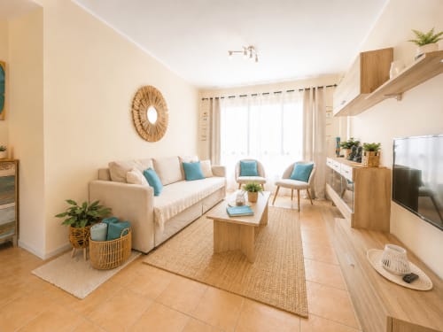 Sala de estar moderna y luminosa en el apartamento Sara & Gino Fuerteventura con sofá beige, muebles de madera, detalles turquesa y televisor