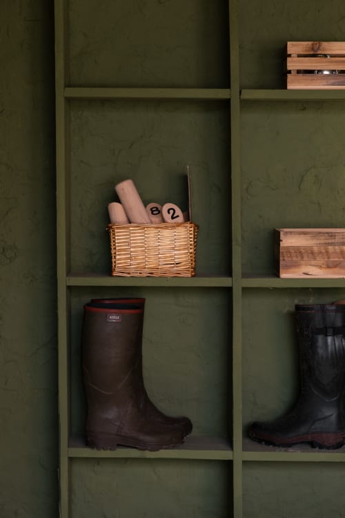 Étagère vert olive à la Guesthouse Moulin Moulin présentant des bottes, paniers et coffres de rangement en bois