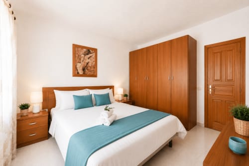 Dormitorio amplio en Sara & Gino Fuerteventura en Corralejo con muebles de madera, ropa de cama blanca, acentos turquesas y armario