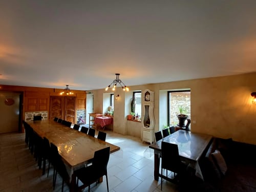 Spacieuse salle à manger aux Gîtes Du Couvent à Nozières avec de longues tables en bois, chaises noires et éclairage chaleureux