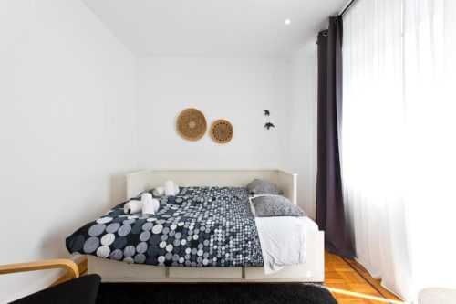 Modern bedroom at Cem Contos Porto with white bed, patterned bedding, woven wall décor, hardwood floors, and curtained
