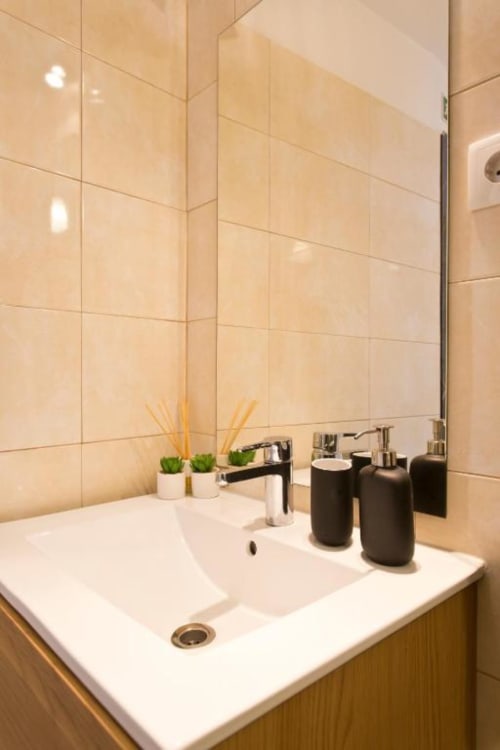 Modern bathroom vanity with white sink, black accessories, and beige tile walls at Cem Contos Porto apartment