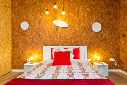 Modern Family Studio bedroom at Cem Contos Porto with cork walls, red bedding, pendant lights, and hardwood floors
