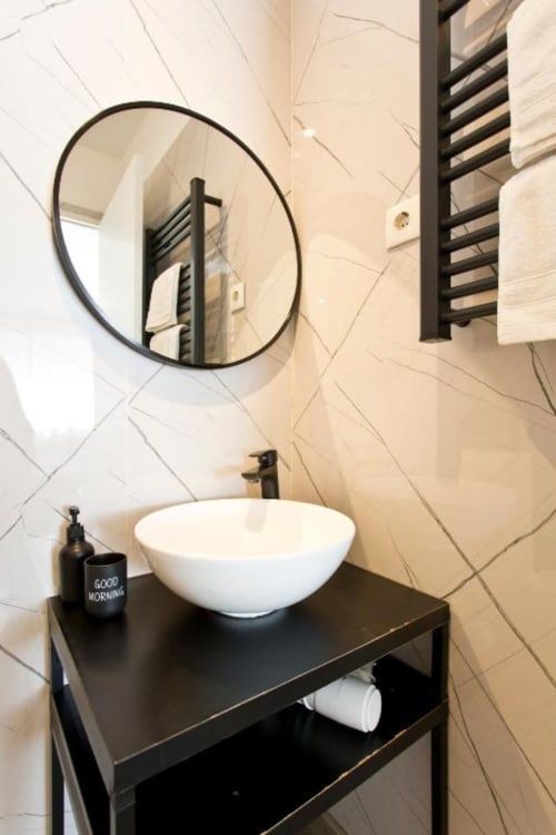 Modern bathroom vanity with round mirror at Cem Contos Porto, featuring white bowl sink and black fixtures