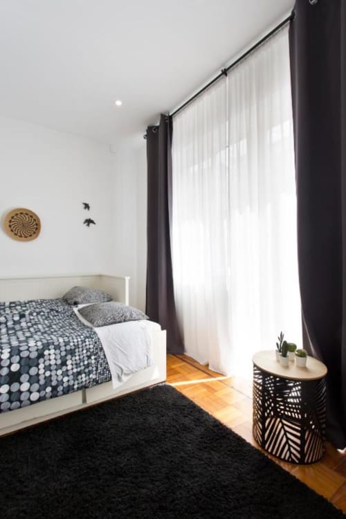 Bright family room at Cem Contos Porto with white bed, dark curtains, wooden floors, and modern minimalist decor