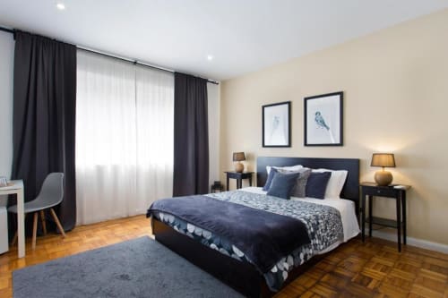 Modern family room at Cem Contos Porto with queen bed, dark headboard, twin lamps, hardwood floors, and cream walls with bird