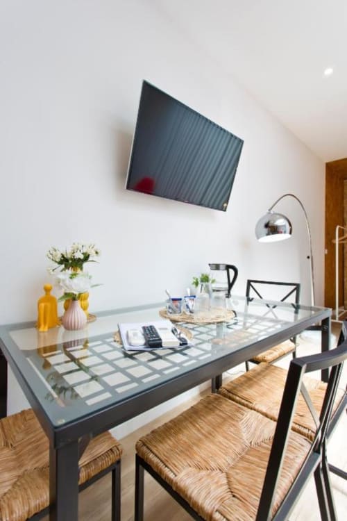 Modern dining area in Cem Contos Porto apartment with glass table, wall-mounted TV, arc lamp, and hardwood floors