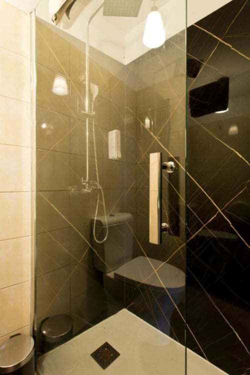 Modern bathroom in Cem Contos Porto family studio with black and beige tiles, glass shower enclosure, and wall-mounted