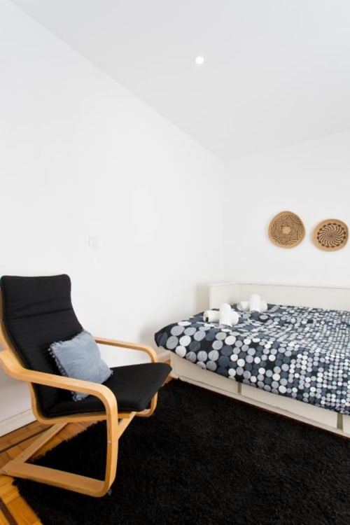 Modern Family Room at Cem Contos Porto featuring wooden chair, white bed with patterned bedding, and minimalist decor