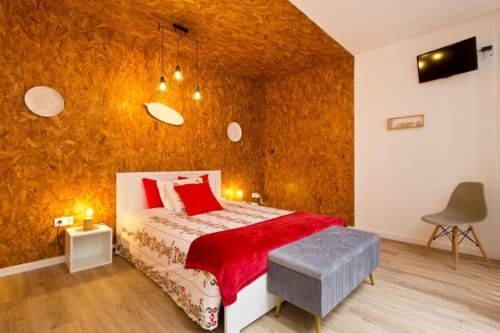 Chambre Bright Family Studio à Cem Contos Porto B&B avec mur en liège, literie rouge, luminaires suspendus et design moderne