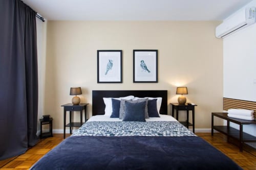 Modern Family Room at Cem Contos Porto with navy bed, twin lamps, bird artwork, and hardwood floors