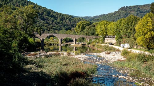 Pont historique en pierre enjambant une rivière avec montagnes boisées au Domaine de Cabrières, St Jean Du Gard