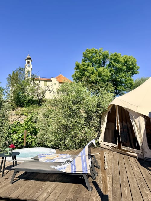 Tente de glamping sur terrasse en bois à l'Agritusmo Stecadò à Dolceacqua, Italie, avec transats, bain à remous et vue sur le clocher