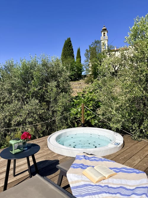 Jacuzzi privé sur terrasse en bois entouré d'oliviers avec vue sur le clocher de Dolceacqua
