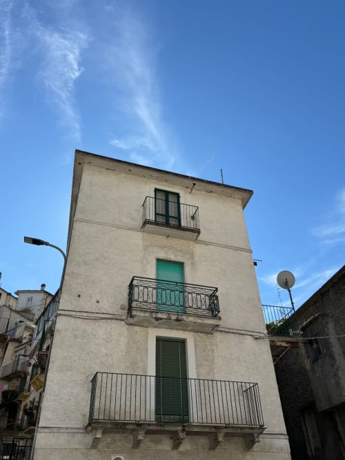 Edificio residenziale color crema ad Atessa, Italia con finestre con persiane verdi e balconate in ferro sotto cielo azzurro