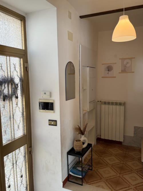 Corridoio moderno in appartamento abruzzese con lampada a sospensione, pareti bianche, radiatore, specchio e stampe botaniche decorative