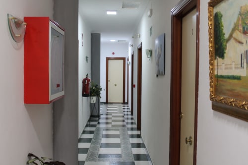 Pasillo del Hostal El Camionero en Burguillos del Cerro con piso a cuadros, puertas de madera y equipo de seguridad contra incendios rojo