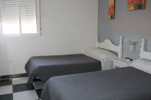 Habitación doble en Hostal El Camionero con dos camas, muebles blancos y vistas a la montaña en Burguillos del Cerro