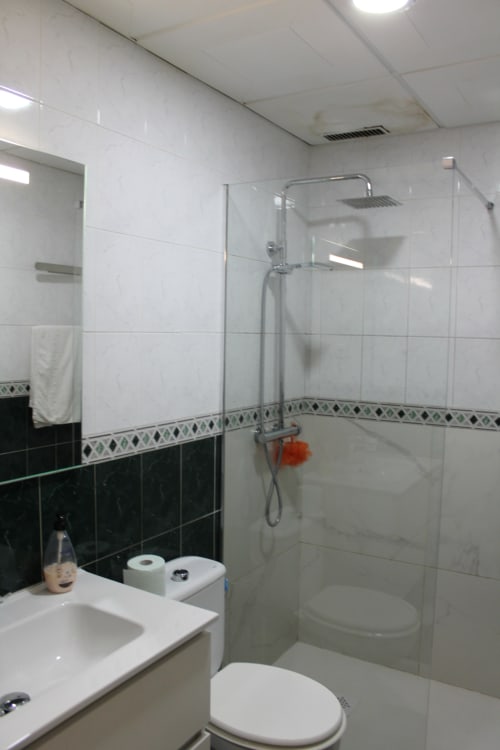 Baño moderno en Hostal El Camionero con mampara de cristal, paredes con azulejos blancos, detalles en azulejos negros, lavamanos e inodoro