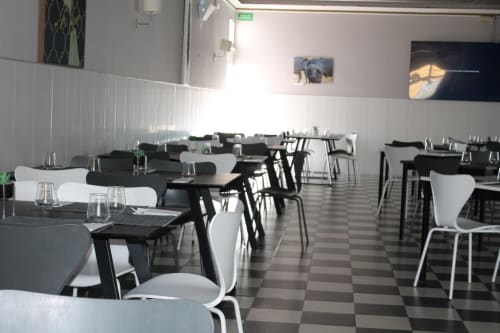 Comedor moderno con mesas negras, sillas blancas y piso de ajedrez en el Hostal El Camionero en Burguillos del Cerro