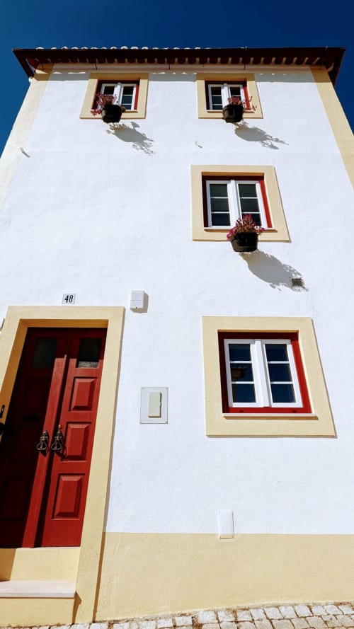Constância Guest House exterior facade with red door, cream walls, yellow trim, and hanging flower baskets