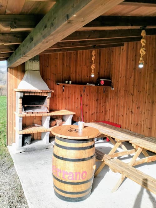 Terraza rústica cubierta en Casa Rural El Serrano con mesa de barril, chimenea de ladrillo y vigas de madera en Prioro