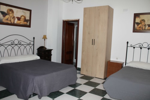 Dormitorio triple en Hostal El Camionero con camas de hierro forjado, armario de madera y piso de azulejos a cuadros en Burguillos del